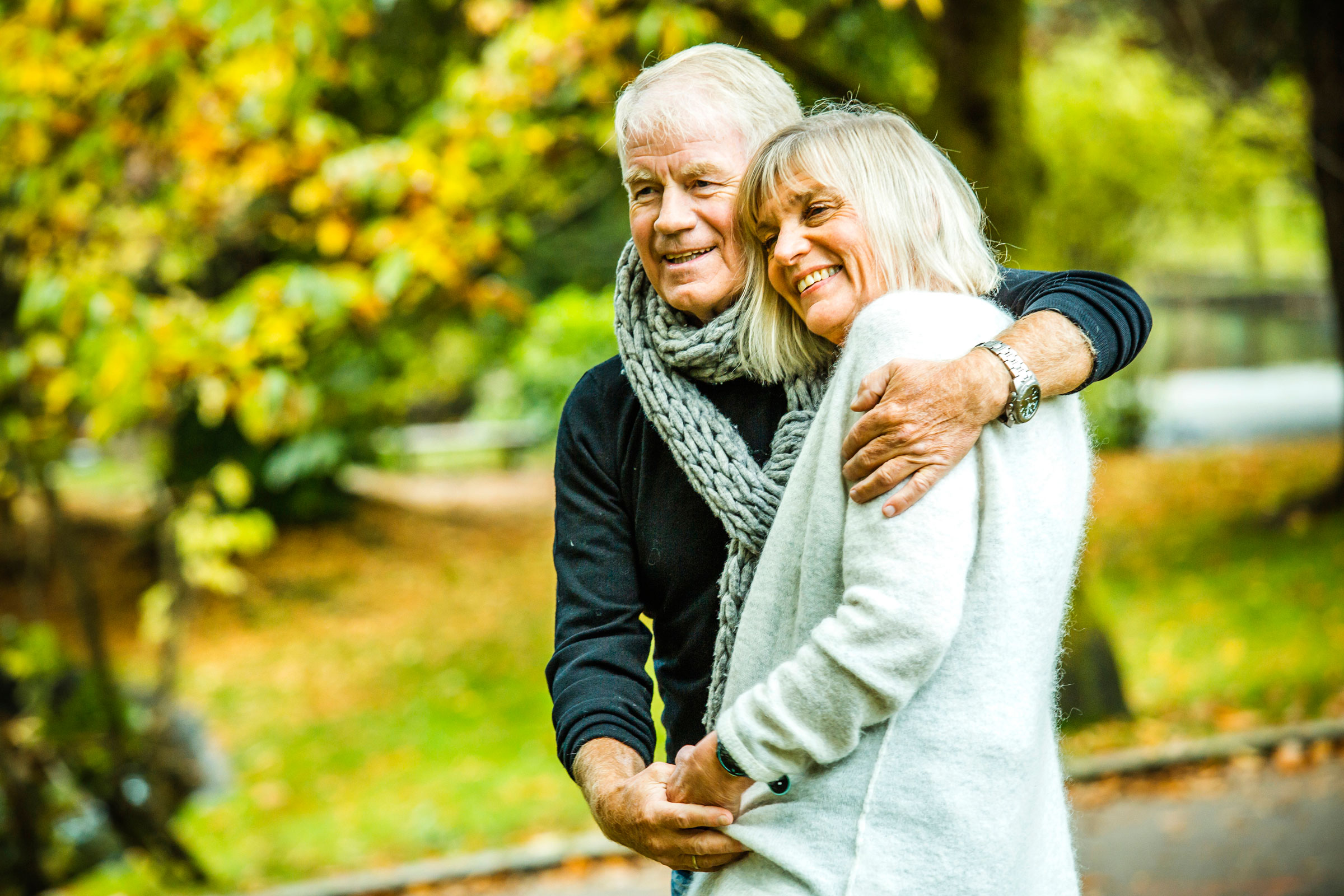 Ældre par står i park og krammer, imens de smiler, fotografi