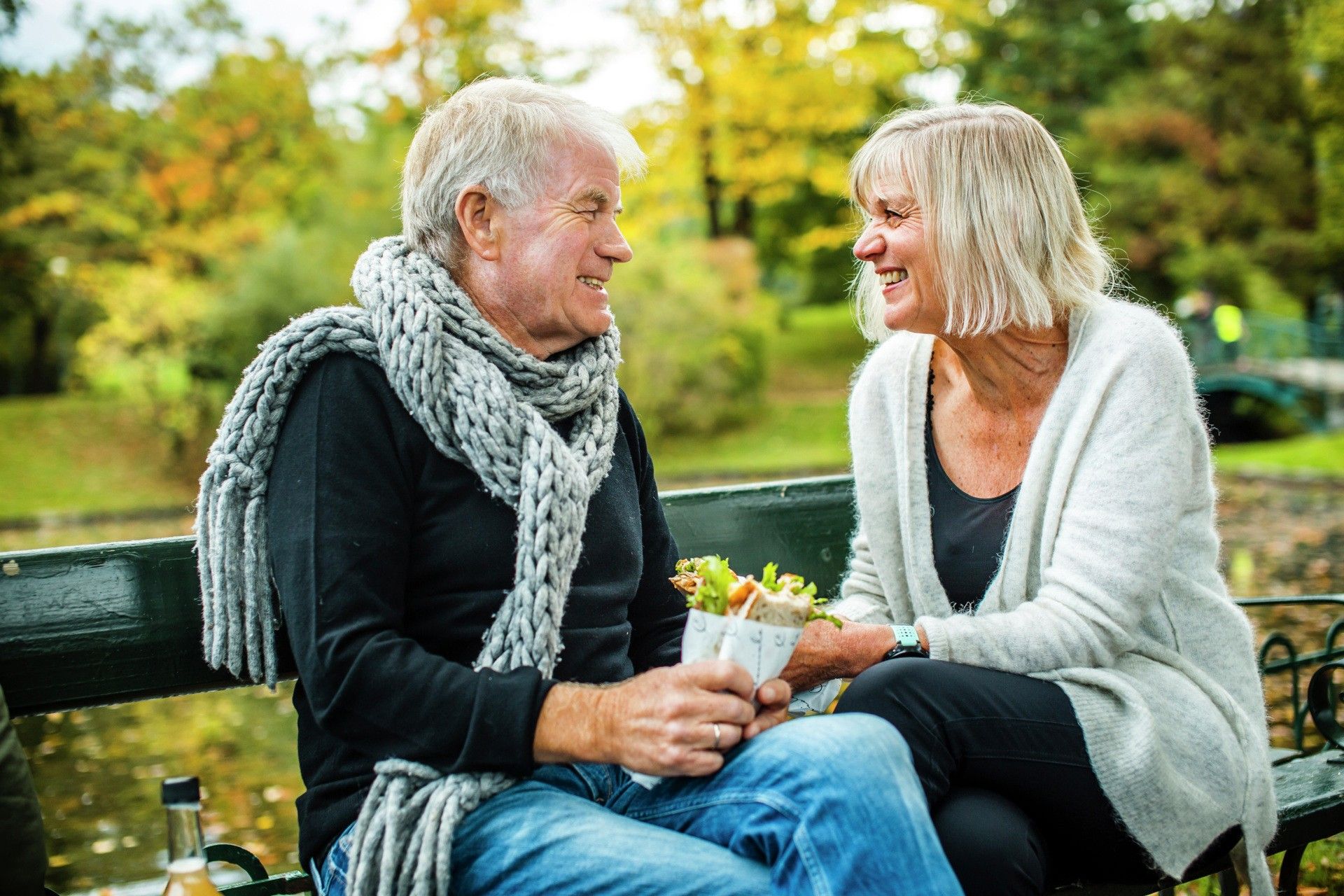 Ældre par sidder på bænk i park og smiler til hinanden, fotografi