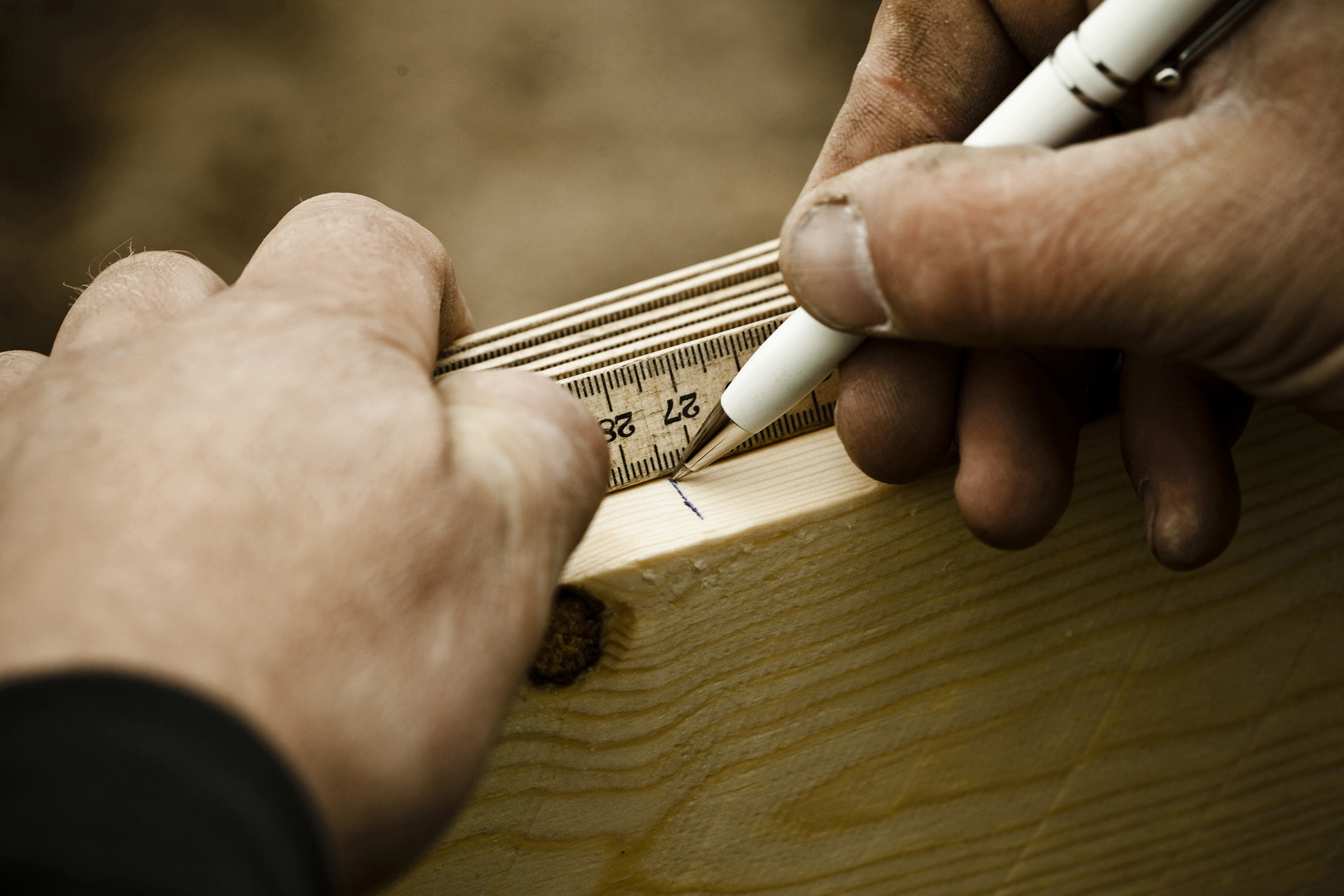 Hænder holder kuglepen og tommestok på et stykke træ og markerer et punkt, fotografi