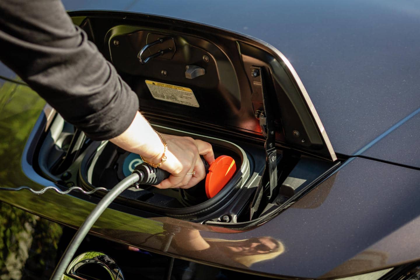 Hånd holder ladekabel og sætter det i stikket på en elbil, fotografi