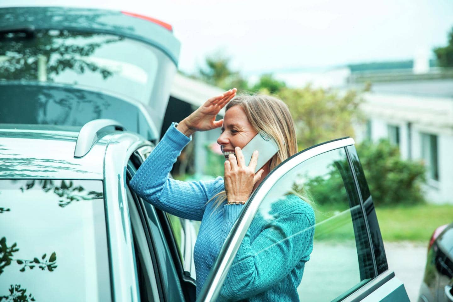 Kvinde ved en bil, der tager sig til hovedet, mens hun snakker i telefon
