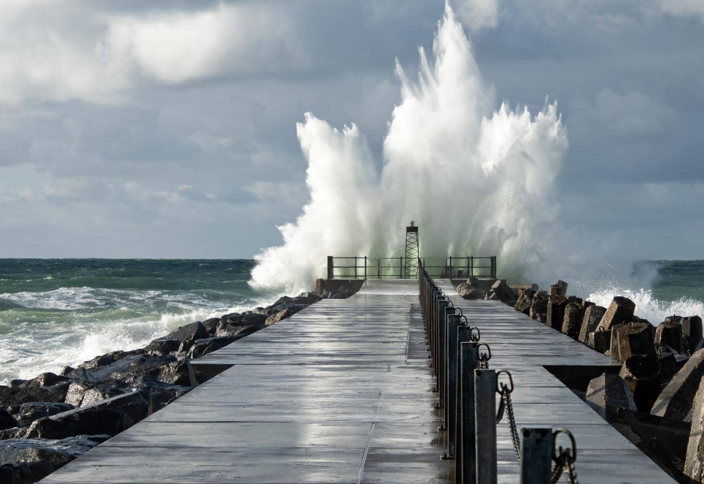 Badebro ved havet, hvor en stor bølge skubber vand op