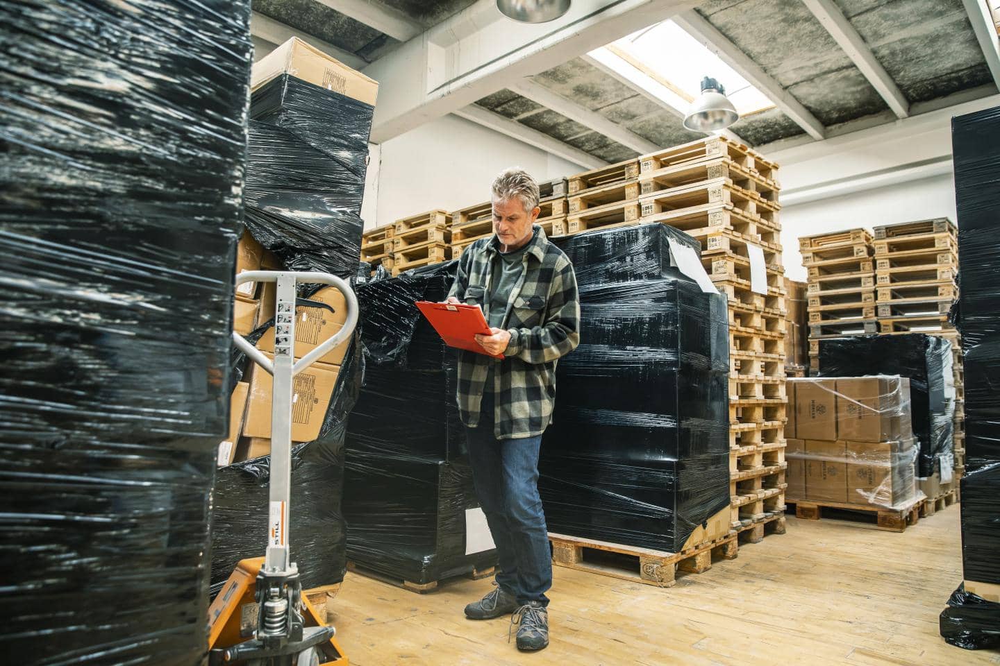 Mand står på et lager med fyldte paller rundt om sig, og noterer på en blok.