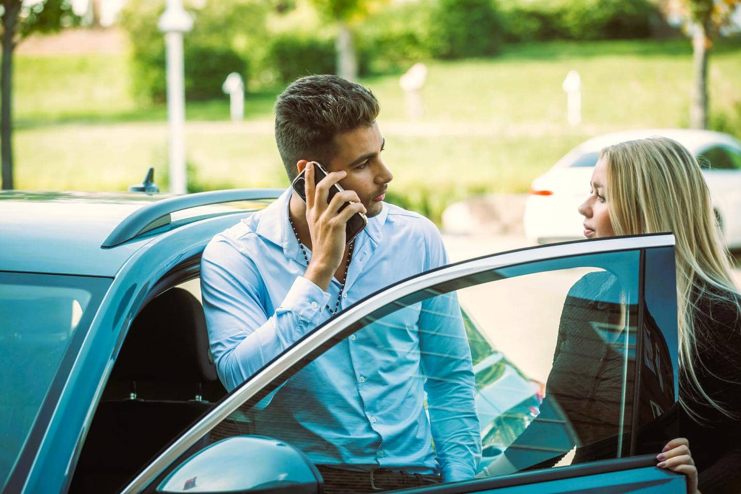 Ung mand og ung kvinde står i døråbning til bil og snakker i telefon